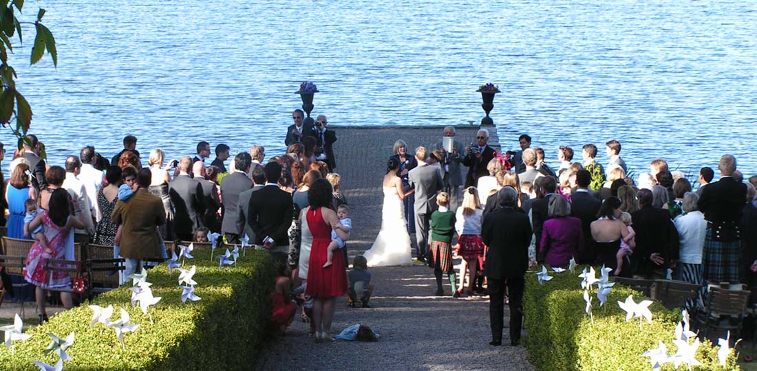 Brudpar viger sig vid stenbryggan med stående bröllopsgäster