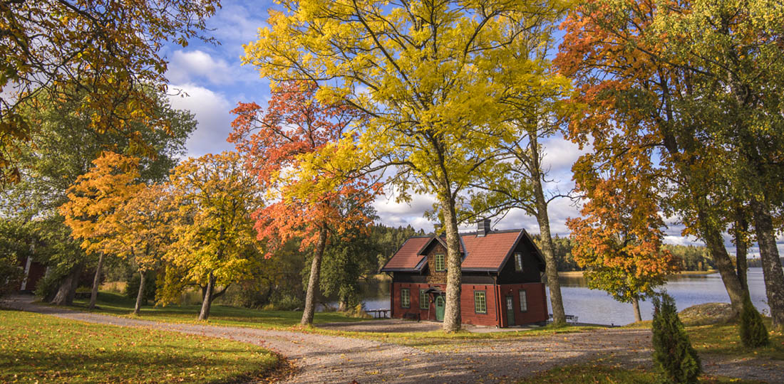 Brygghuset. Rött och svart hus vid sjön Båven. Träd med höstfärger