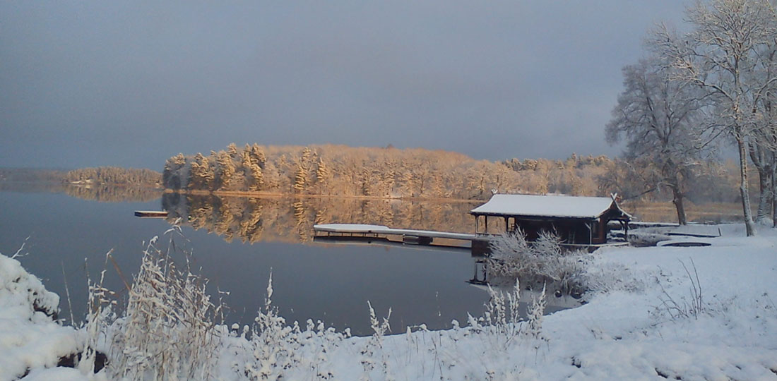 Sjöbastu i vinterlandskap med solbelyst skog vid sjön
