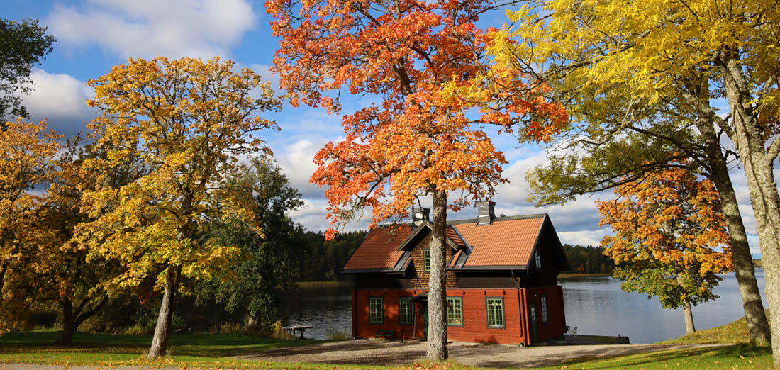 Brygghuset är ett rött hus vid sjön. Röda höstfärger på träden