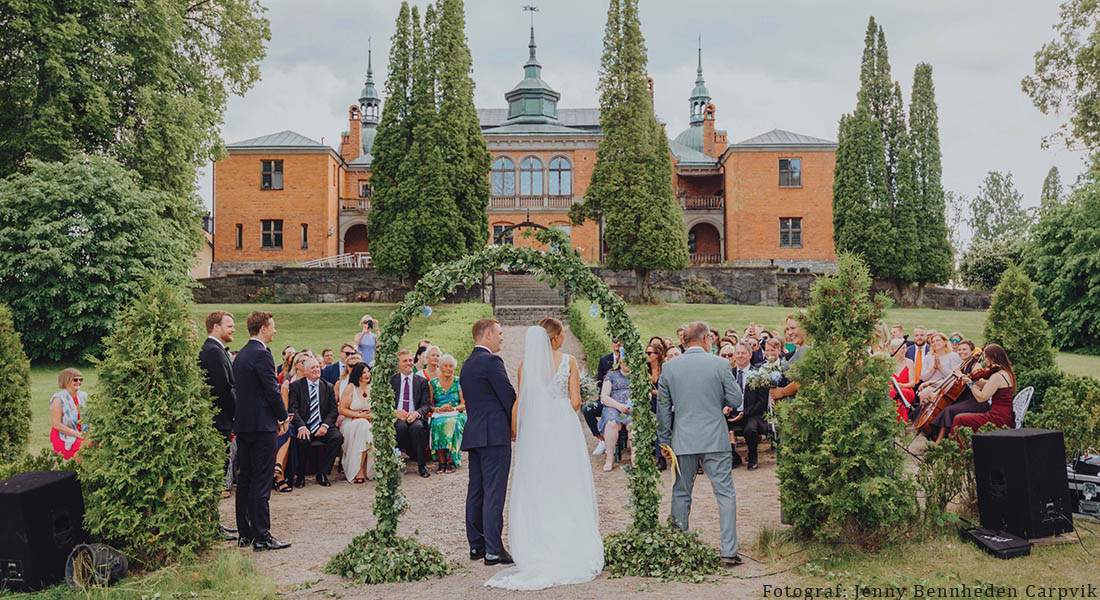 Vigsel med lövad båge och slottet i bakgrunden av fotograf Jenny Bennheden Carpvik