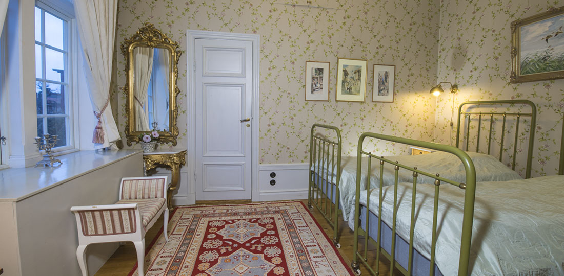 Sovrum med gröna sängar, guldspegel och blommiga tapeter