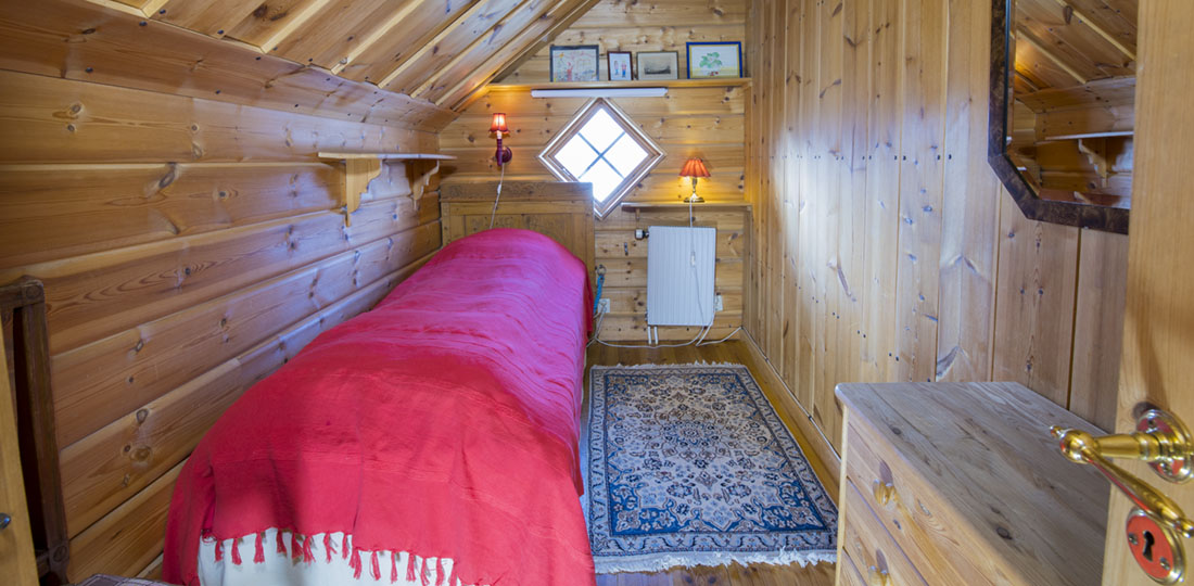 Litet sovrum med träväggar, rött överkast och antik matta